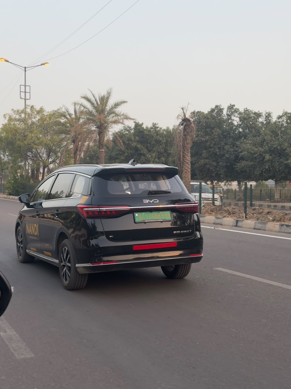 A black BYD eMAX 7 seen from behind on a tree-lined road.