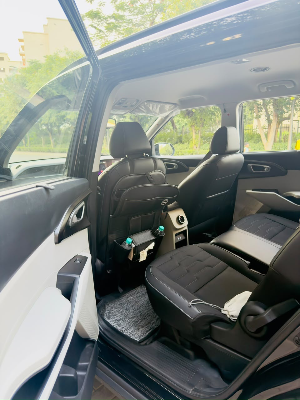 A Kia Carens with its rear door open: second-row seats and a seat-back organiser holding water bottles and tissues.