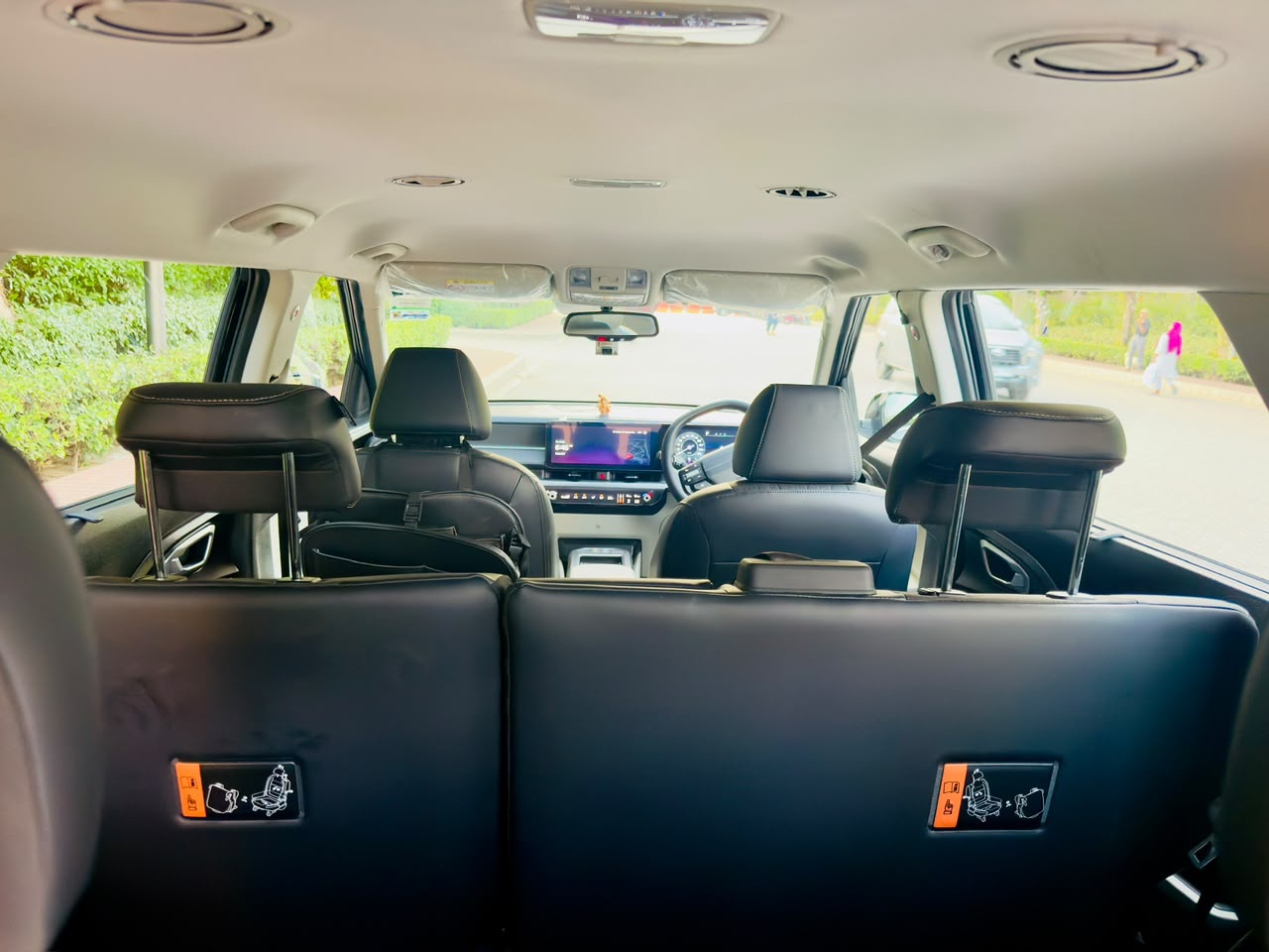The interior of a Kia Carens looking forward from the third row: black leather-style seats with white stitching and roof vents.